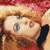 Pixelated close-up of a character with light brown hair, blue eyes, and a red garment, set against a blurred background with warm tones.