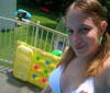 A person with light brown hair in a white sleeveless top stands near a yellow inflatable structure with colorful circular patterns on grassy ground.