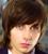 Static pixelated image of a person's face with brown hair and light skin tone, cropped closely to show only the upper portion of the head against a blurred background.