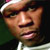 Pixelated close-up of a person's face wearing a light-colored cap, with visible skin tones and dark background.