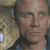 A pixelated image of a person with short light hair, blue eyes, and a neutral expression, wearing a dark jacket over a light shirt against a blurred background.