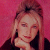Static pixelated image of a person with light brown hair against a solid pink background, wearing dark clothing and resting a hand near the chin.