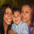 A static image of two adults and a child in a close group pose, with one adult holding the child, all smiling against a dark background.