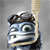 Pixelated cartoon character with large green eye, dark brown hair, and light blue face holding a long beige object against gray background.