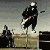 Pixelated image of a person with light hair and dark sunglasses in foreground, another figure on horseback in background.