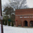 Pixelated static image of a brick building with arched doorways, a tree, and a street sign partially visible on the left.