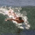A person in a white top and brown shorts swims in dark green water with white foam, viewed from above.