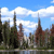 Pixelated landscape with blue sky, white clouds, and dark green trees reflected in water.