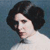 Pixelated portrait of a person with dark curly hair wearing a white top against a blue background.