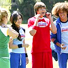 Four people stand outdoors in a grassy area with trees in the background; one person in red holds a phone to their ear.