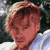 Pixelated static image of a person's face with light brown hair and red skin tones, wearing a blue shirt against a dark background with white highlights.