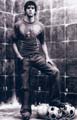 Black-and-white static image of a shirtless man leaning against a brick wall with soccer balls at his feet, rendered in low-resolution pixelated style.
