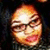 Pixelated close-up of a smiling person with glasses, warm orange and yellow tones, dark background, static image.