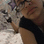 A person with glasses and a black sleeveless top lies on patterned fabric, holding a plush toy with purple accents.