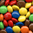 Pixelated image of colorful chocolate candies with two text blocks on dark brown background.