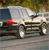 A pixelated image of a white sedan with a red roof light, positioned on a road with blurred background elements.