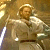 Pixelated static image of a character in light-colored attire with brown hair and beard, holding an object against a warm-toned background.