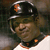 Pixelated image of a person wearing a dark helmet with orange accents and a green uniform, viewed from the side.
