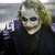 A character with white face paint, red lips, and dark eye makeup wears a purple shirt under a black coat in three