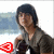 Pixelated image of a person with dark hair wearing a gray sleeveless top, holding an object near their chest against a light background.