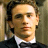 Pixelated portrait of a person with light skin tone wearing a dark suit jacket and white dress shirt, set against a muted brown background.