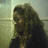 Pixelated static image of a person with long dark hair wearing dark clothing against a light background.