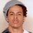 Pixelated close-up of a person with light brown skin, dark brown curly hair, and closed eyes, wearing a dark top against a light background.