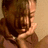 A pixelated image of a person with brown hair holding their hands near their face, wearing a light-colored top and necklace.