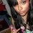 A pixelated close-up of a person with dark hair wearing a black top and pink accents, holding an object near their chest.