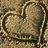 A heart-shaped sand drawing on a textured surface with pixelated text reading "Soon It Gets Washed Away" in pink letters against a light purple background.
