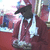 A pixelated figure in a red outfit with white accents stands against a red background, holding a dark object near its face.