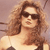 A pixelated image of a person with long brown hair wearing dark sunglasses and a light-colored top against a muted background.