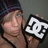 A person wearing a dark beanie holds up a white and black DC logo against a gray background, with blue text reading SEXY! appearing in the top right corner.