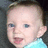 Pixelated close-up of a child's face with light skin, blue eyes, and short brown hair, wearing a light blue garment against a dark background.