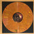 Circular orange-brown disc with dark central spiral and light reflection, set against dark background with subtle color gradients.