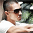 A man in a white shirt and dark sunglasses appears in a of four with a blurred green background