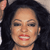 Pixelated close-up of a person with dark curly hair, light skin, and red lips, wearing a dark top against a blurred background.
