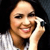 A pixelated close-up of a person with light skin tone holding a white phone to their ear, wearing a white and gray checkered shirt against a dark background.