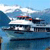 Pixelated static image of a white boat on blue water with a light blue sky and white clouds, featuring a pink and red detail on the boat's upper structure.