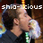 Pixelated image of a person with dark hair holding a microphone, overlaid with white text reading 'shio-licious' against a dark background.