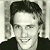 Black-and-white portrait of a smiling person with dark hair against light background, adjacent to green text reading 'Original Icons .com' in pixelated font.