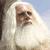 Pixelated image of a person with long white hair and beard, wearing light-colored clothing, against a blue sky background.