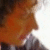 Pixelated image of a figure with brown hair and orange clothing against a light background, cropped at the edges.