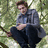 A person in a gray jacket and dark pants sits on a tree branch with green foliage background, overlaid with text elements.