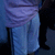 A person in light blue pants and a purple garment stands against a dark background with a white area on the right.