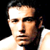 Static pixelated close-up of a person's face with dark hair and light skin against black background, wearing white garment.
