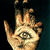A hand with an eye symbol on the palm, rendered in warm tones against a dark background.