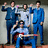 Group of five people in blue suits with one seated person holding a red guitar, transitioning from no text to pink 'hello goodbye' text overlay.