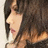 Pixelated close-up of a person with long dark hair, light skin, and a white top, cropped to show upper body and hair against a light background.