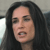 Pixelated close-up of a person with long dark hair, light skin, and an open mouth showing teeth, set against a blurred background with light and dark areas.